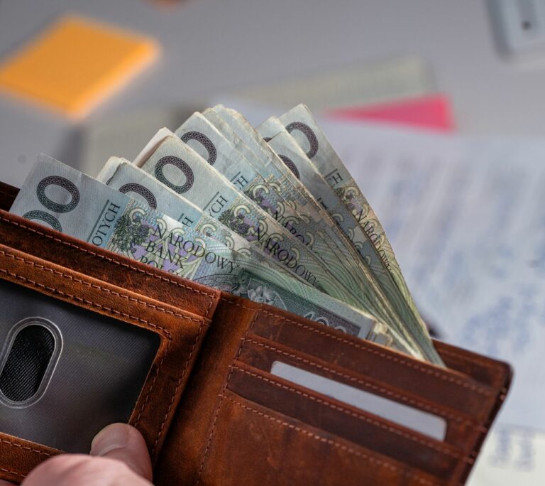 Brown leather wallet containing Polish zloty banknotes on cluttered desk