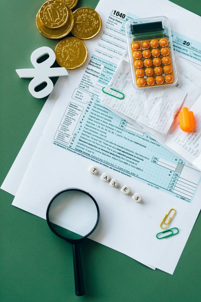 Top view of tax forms, calculator, coins, and office supplies on a green desk.
