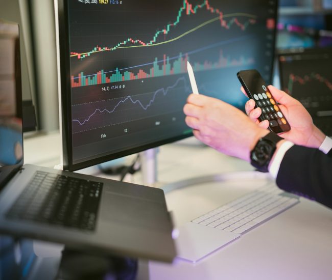 A professional analyzing financial charts on computer monitors and a smartphone, symbolizing digital finance strategies.