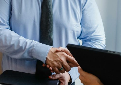 Business handshake between colleagues in a formal office meeting setting.