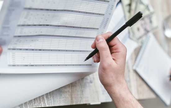 A close-up of a person holding a pen reviewing a financial document with cash visible, ideal for business themes.